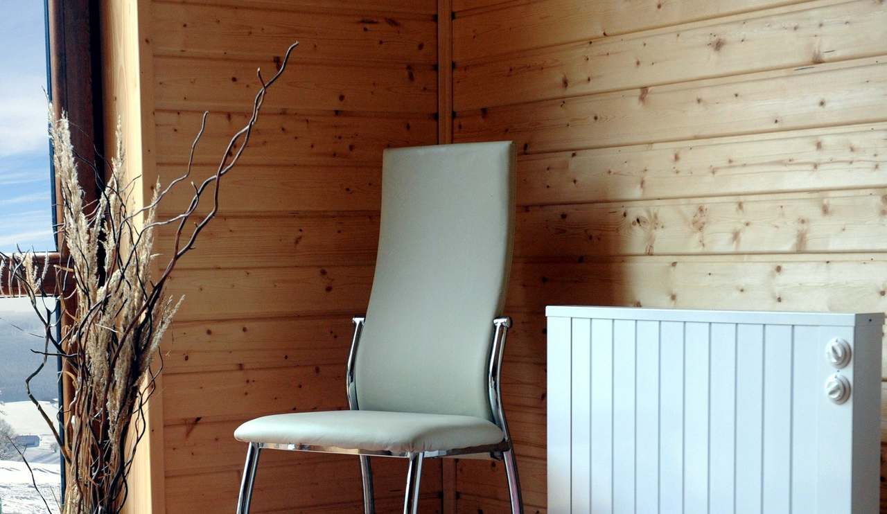 Witte Jawotherm radiator tegen een houten wand naast een stoel